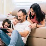 Parents sitting with their children, guiding them as they use gadgets together.