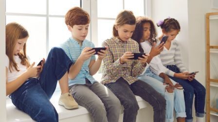 Kids sitting next to each other, each absorbed in their phone, showing a lack of interaction or engagement with one another.