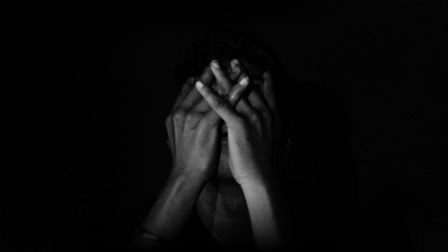 A person sitting in the dark, covering their face, expressing sadness, stress, or contemplation.